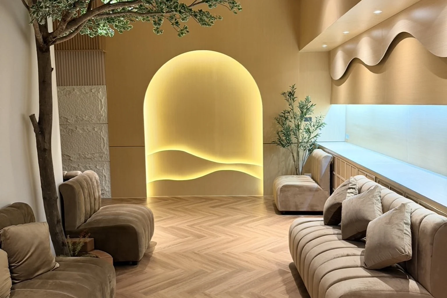 ล็อบบี้จริงของ QQ SPA พร้อมซุ้มไฟ ต้นไม้ภายในอาคาร และที่นั่งไม้โอ๊กสีอ่อน